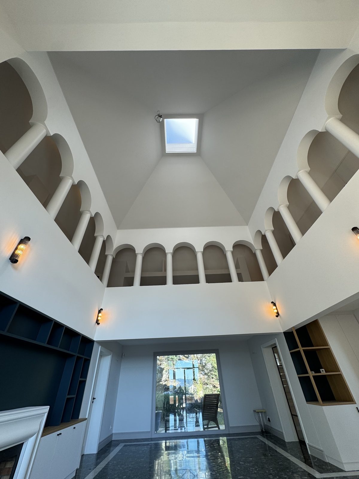 Le même séjour cathédrale une fois terminé : arches et plafond peints, sol en marbre, bibliothèque bleu nuit