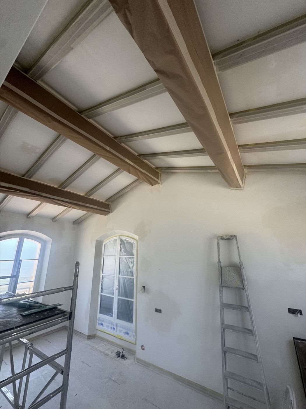 Pièce sous charpente aux poutres et plafond repeints, fenêtre cintrée